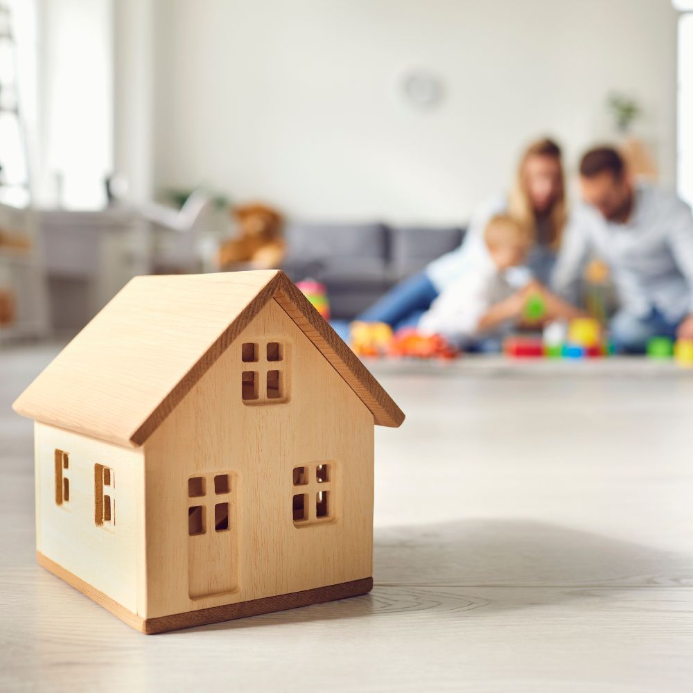 Small wooden home placed on the floor with a family sat in the background