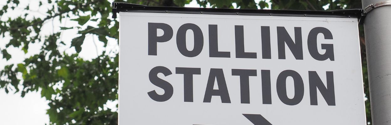 Image of polling station sign on a metal pole with trees in the background