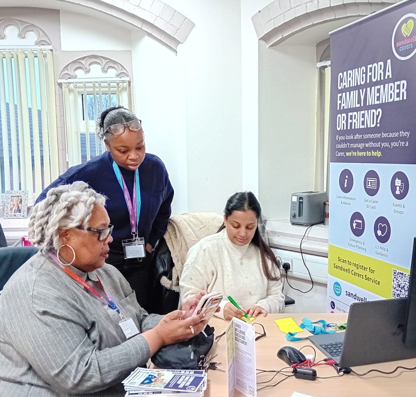 image of Cllr Taylor accessing the carers' Bridgit App on her phone, along side members of the Carers Service